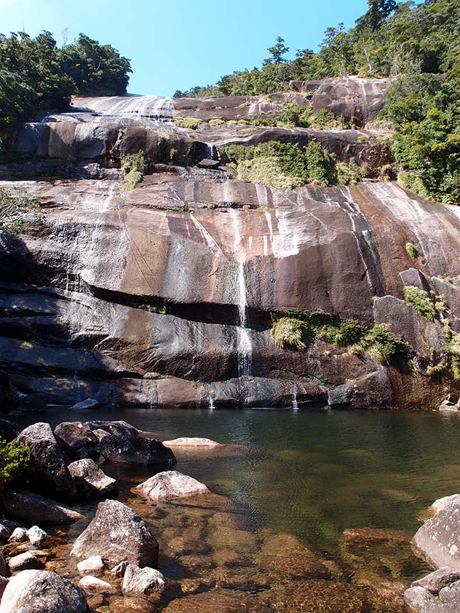 The Jyanokuchidaki Falls. Clear water gently flows over the smooth granite rock surface of the falls.