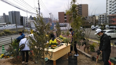 道路脇のスペースで作業しています。中央には木で作られた花壇も見えます。