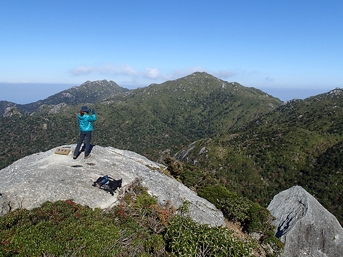 A hiker on the peak of Mt. Kuromi looks out over the magnificent Mt. Miyanoura and Mt. Nagata. The lush vegetation of the mountains.