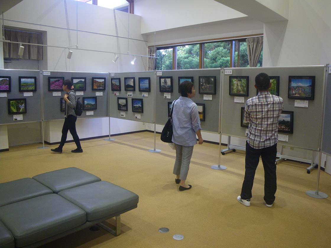 遺産センター内で開催された、九州地区アクティブ・レンジャー写真展の様子。たくさんの写真が掲示され、数名の来館者が写真を見ています。