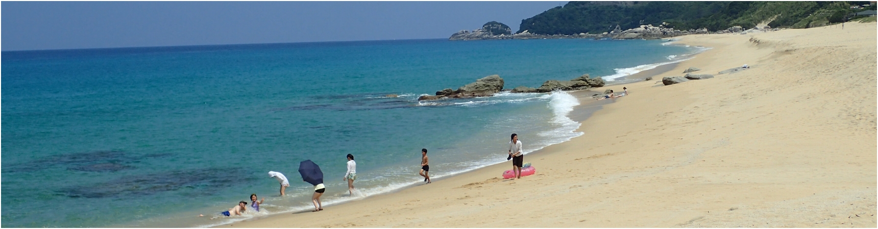 青い海と砂浜が美しい永田浜の写真。数名の人たちが、海水浴を楽しんでいます。