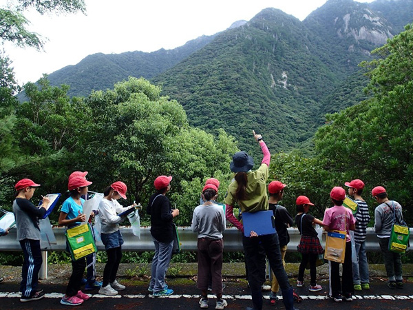 アクティブ・レンジャーが、西部地域の森で、小学生を対象に、屋久島の自然環境の魅力や大切さを伝えるための出前授業を行っている風景。
