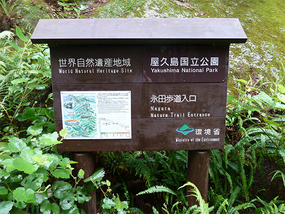 永田歩道入口に設置された、案内標識の写真。標識の板面には、永田歩道入口、世界自然遺産地域、屋久島国立公園の文字があり、左下には登山道の地図が張られています。